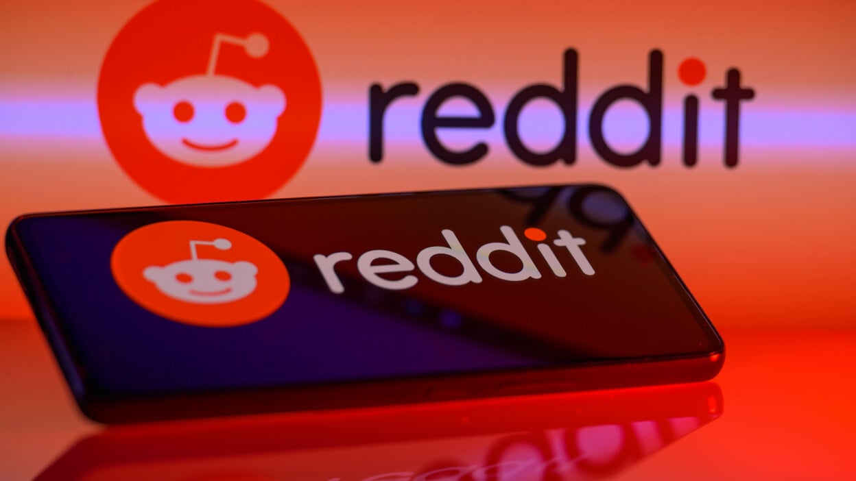 The reddit logo reflected on an iPhone screen and glowing red backdrop.