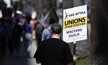 A protester in a black shirt and black baseball cap carries a picket sign that reads, "Unions stand together. SAG-AFTRA supports writers guild."
