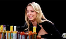 A woman sits at a table in a dark room with sauce bottles in front of her.