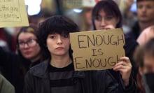 A young person holds up a cardboard sign that reads "Enough is enough."