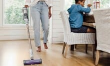 a person vacuums a wood floor with the shark detect pro cordless vacuum near a table where a child is sitting and eating