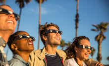 four people wearing eclipse glasses smile while looking into the sky