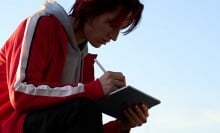 a person sits cross-legged outside while using an apple iPad air tablet with an apple pencil