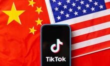 A mobile phone displays TikTok logo with the flags of United States of America and People's Republic of China in the background.
