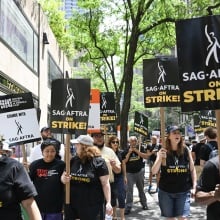 A group of striking people in black shirts holding signs that say "SAG-AFTRA on strike!" walk the streets of New York.