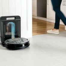 a robot vacuum is at its dock, emptying, while someone walks by on the right side