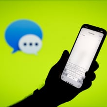  Apple iMessage app open on phone in front of green backdrop with iMessage logo