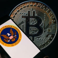 The seal of the U.S. Securities and Exchange Commission is being displayed on a smartphone, with Bitcoin visible on the screen in the background.