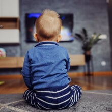 A young child watches a TV screen.