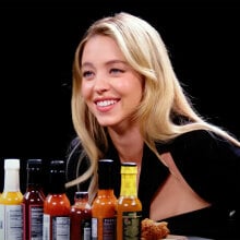 A woman sits at a table in a dark room with sauce bottles in front of her.