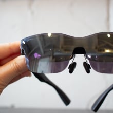 woman's hand holding dark, reflective XR glasses
