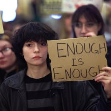 A young person holds up a cardboard sign that reads "Enough is enough."