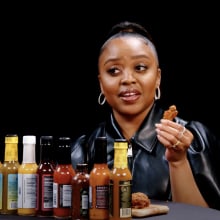 A woman sits at a table in front of a row of sauces.