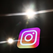 The Instagram logo on a black background. Bright camera flashes light up around it.