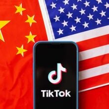 A mobile phone displays TikTok logo with the flags of United States of America and People's Republic of China in the background.