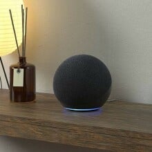 an amazon echo speaker sits on a side table with dim light and a scented oil diffuser next to it