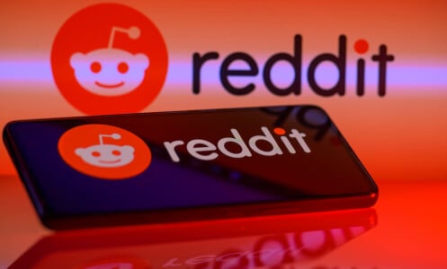 The reddit logo reflected on an iPhone screen and glowing red backdrop.