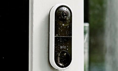 the arlo essential wired video doorbell on the site of a house while its raining