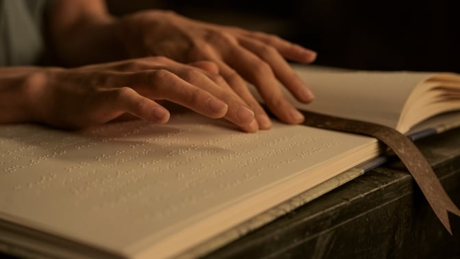 A pair of hands glide over lines of braille in a book. 