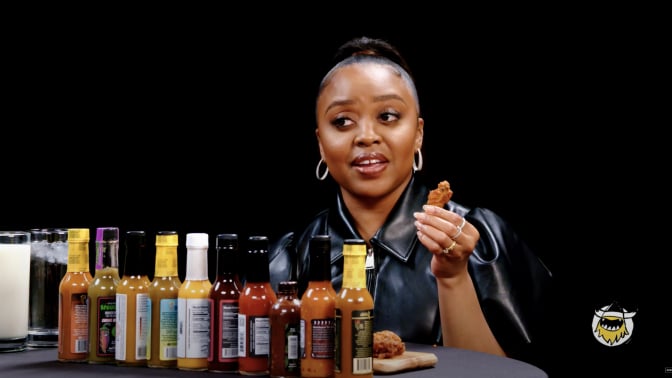 A woman sits at a table in front of a row of sauces.