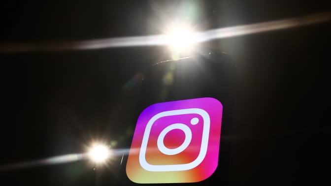 The Instagram logo on a black background. Bright camera flashes light up around it.