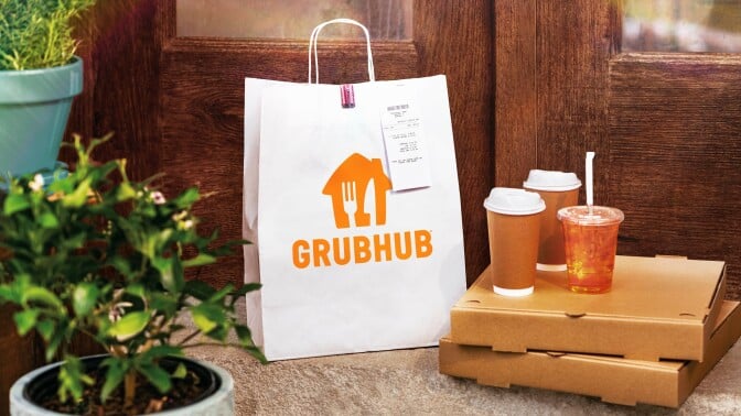 a white paper grubhub bag sits on a front porch next to two pizza boxes that have three drinks on top