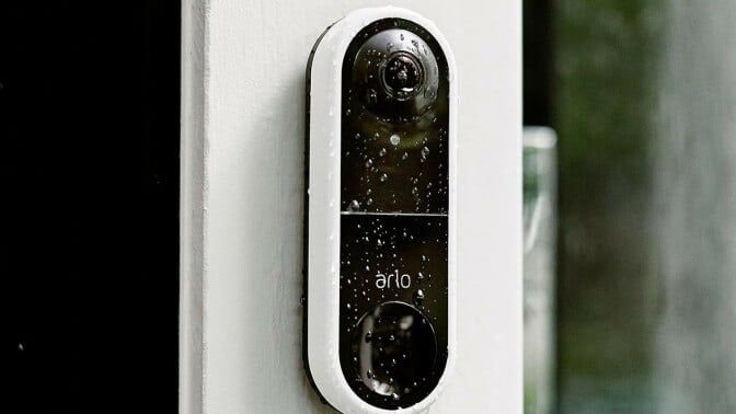 the arlo essential wired video doorbell on the site of a house while its raining