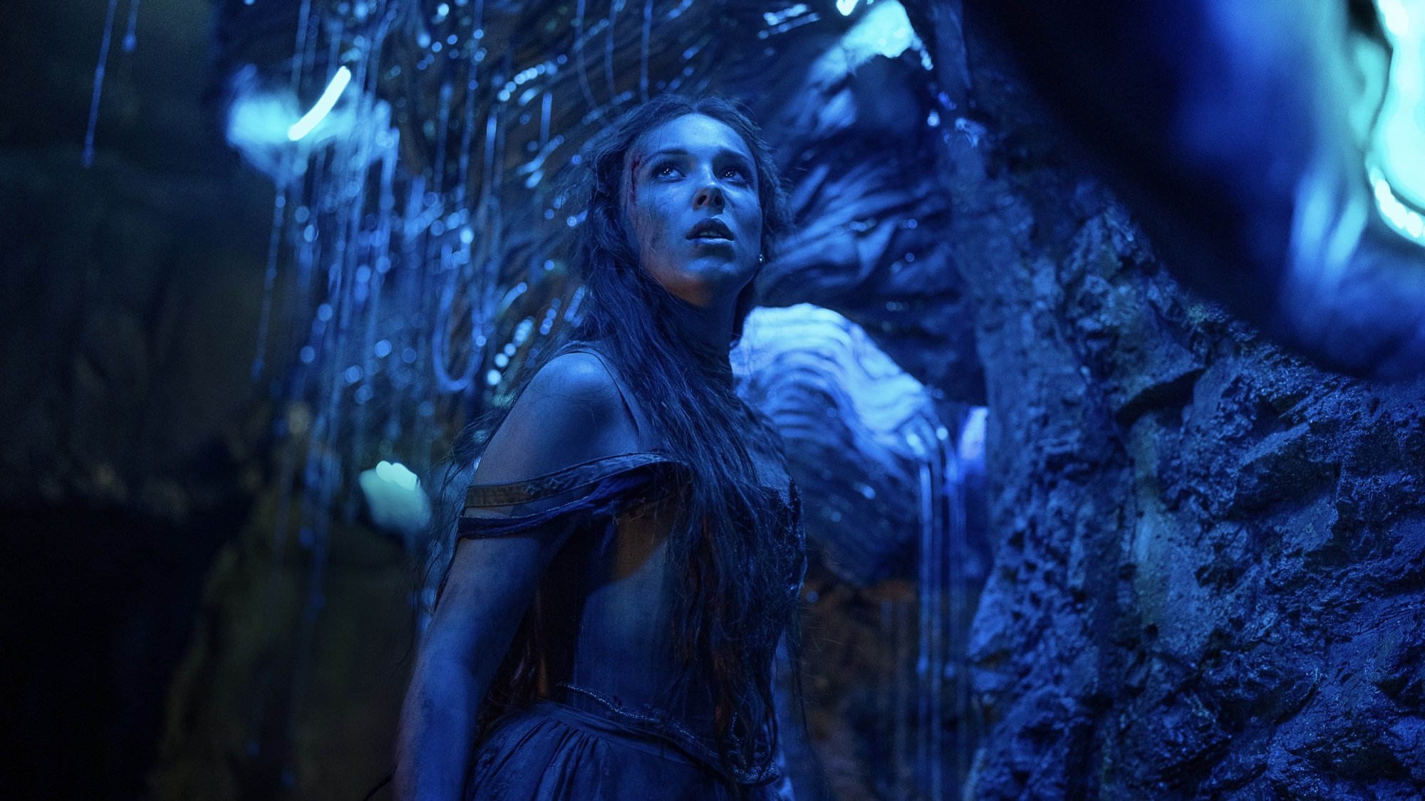 A young woman stands in a cave lit blue by glowworms.