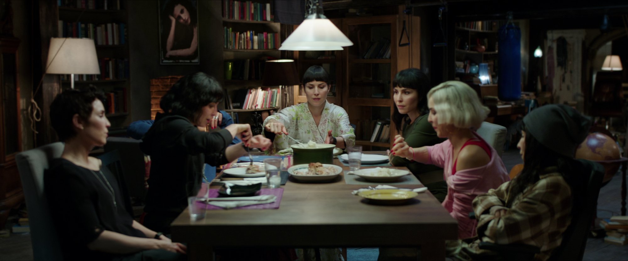 Six identical women sit around a dinner table.