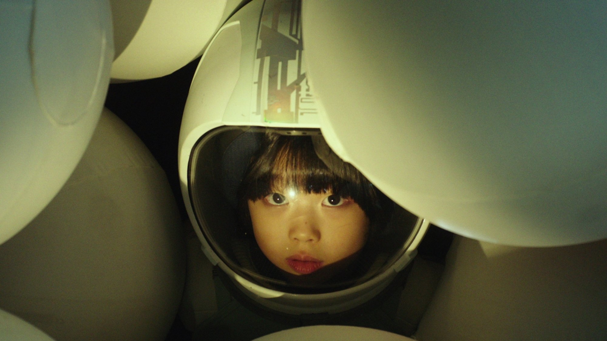 A small girl in a space helmet stares at the camera.