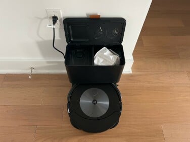 Roomba on charging dock with lid lifted to show automatic empty bag inside