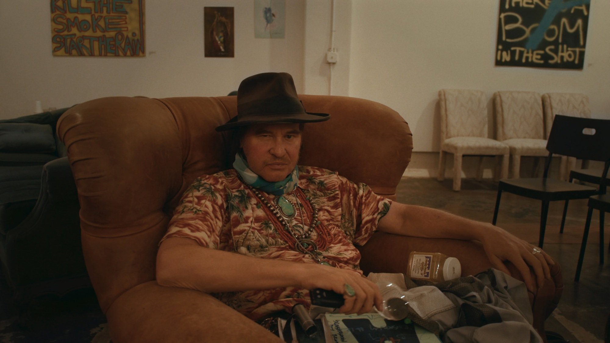Val Kilmer sitting in a brown armchair.