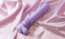 purple thrusting dildo lying on bed sheets