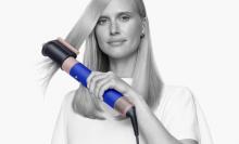 Woman styling her long, blonde hair with the Dyson Airwrap while staring at the camera