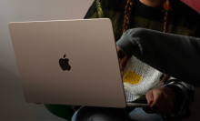 a close-up of a woman holding a 15-inch apple macbook air while another person points at its screen