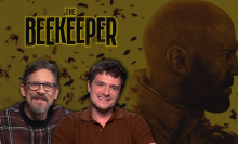 osh Hutcherson and David Ayer smile at the camera. A giant yellow poster of the 'Beekeeper' with a close up of Jason Statham standing among a swarm of bees is their background.