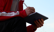 a close-up of a person writing on an apple ipad air with an apple pencil outside