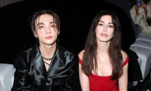 Hyunjin and Anne Hathaway sit side by side. He is in a black leather jacket and she is in a red dress.