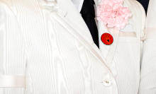 A zoomed-in photo of Phoebe Bridgers' white suit lapel, with a pink flower and a red "ceasefire now" button pinned to it.