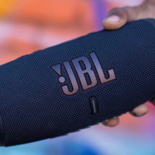 a close-up of a person holding a jbl charge 5 in front of a colorful wall