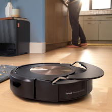 Roomba cleaning hardwood floor and lifting mopping pad with person and iRobot dock in background
