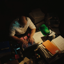A man looks over a stack of papers in a dimly-lit attorney's office. 