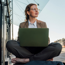 Thoughtful businesswoman sitting cross-legged with laptop on bench