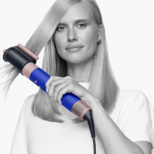 Woman styling her long, blonde hair with the Dyson Airwrap while staring at the camera