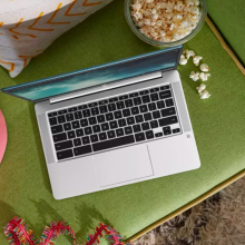 a top-down view of an hp chromebook sitting on an olive green couch next to a pink guitar and a spilled bowl of popcorn