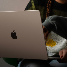 a close-up of a woman holding a 15-inch apple macbook air while another person points at its screen