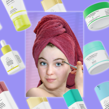 A young white girl with a terry towel wrapped around her hair list a makeup brush to her eye. Around her are a rainbow array of Drunk Elephant products.