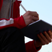 a close-up of a person writing on an apple ipad air with an apple pencil outside
