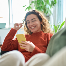 Happy relaxed young woman sitting on couch using cell phone