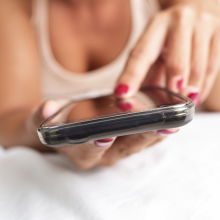 closeup of a young caucasian woman face down in bed using a smartphone